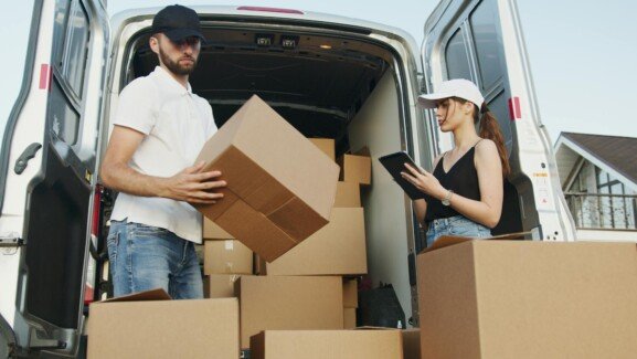 A man and woman stand by a moving van, discussing the costs of international moving.