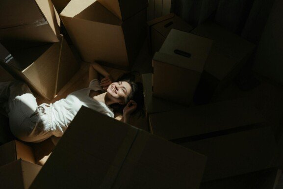 A woman rests on a pile of cardboard boxes, preparing for her move overseas.