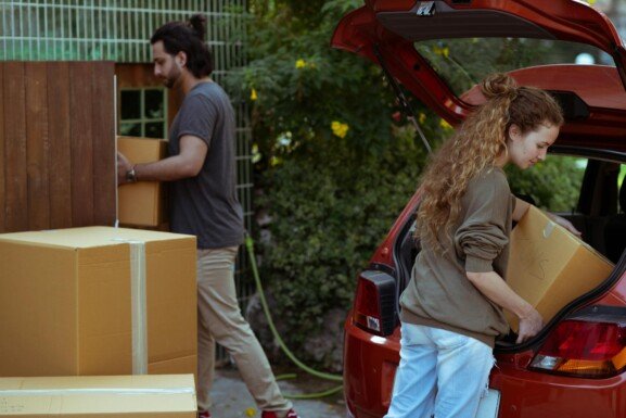 A man and woman taking boxes out of a car, readying for their long-distance moving process.
