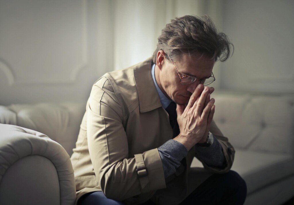  A man in a trench coat is engaged in prayer, expressing his wish to move to the US for new opportunities.